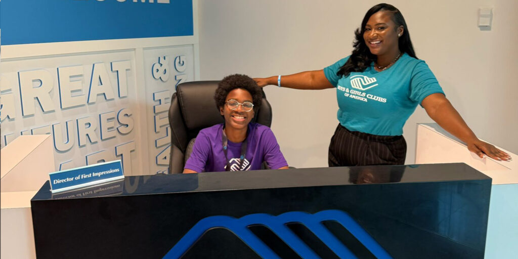 Jakeclaude smiling sitting behind a Boys and Girls Club Desk alongside a Boys and Girls Club Staff member.