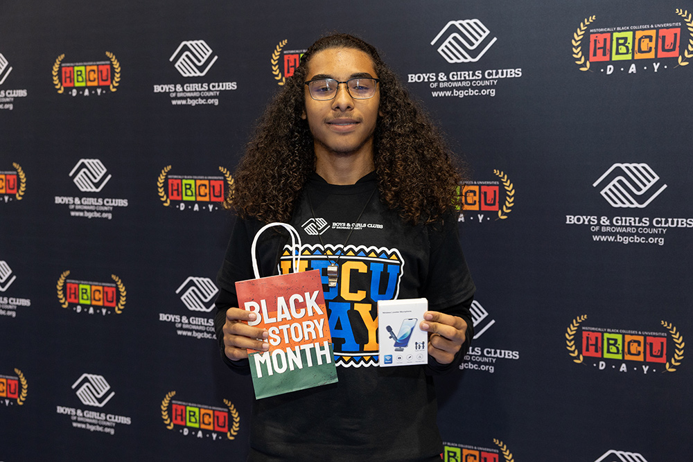 A BGCBC Club Member holding a gift bag that reads 'Black History Month' along with a new phone mircophone