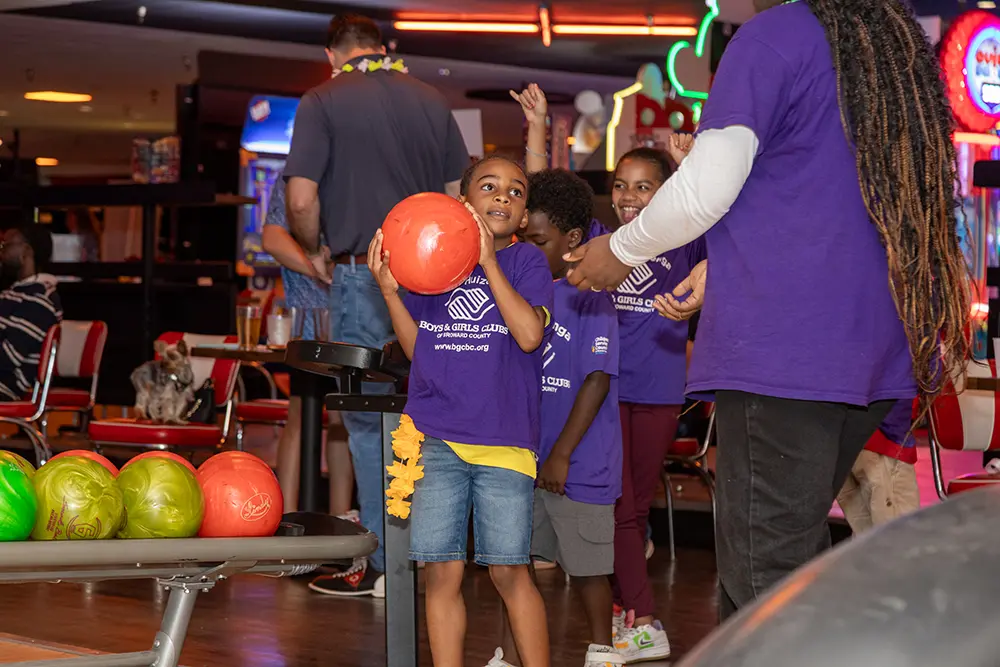 A BGCBC club member wearing a Boys & Girls Club of Broward County shirt and holding a bowling ball