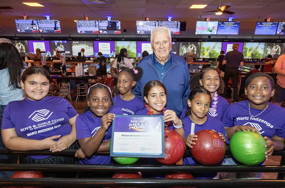 An attendee and Seven BGCBC Club members posing with their certificate from the Bowling for Kids event standing behind Bowling balls.