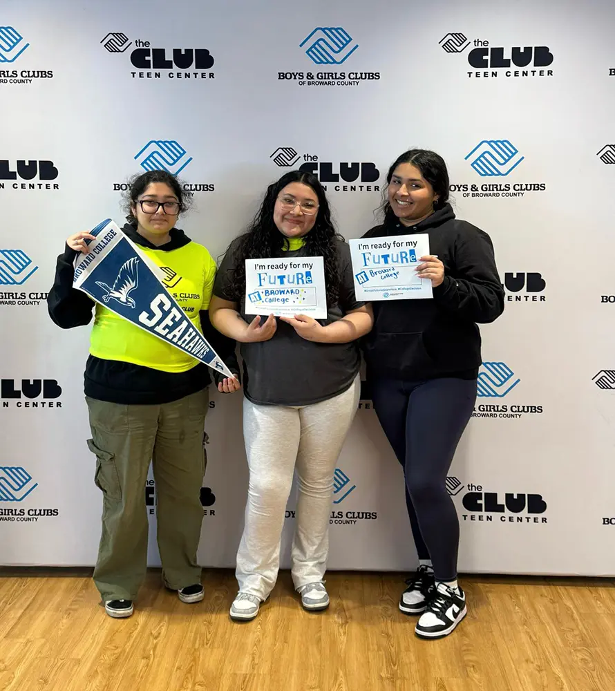 Two BGCBC club members holding their signs that read "Broward College". A third club member holds up a Broward College pennant that reads 'Seahawks'.