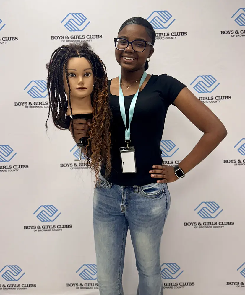 A participant of the Hair braiding program proudly showcasing their training head.