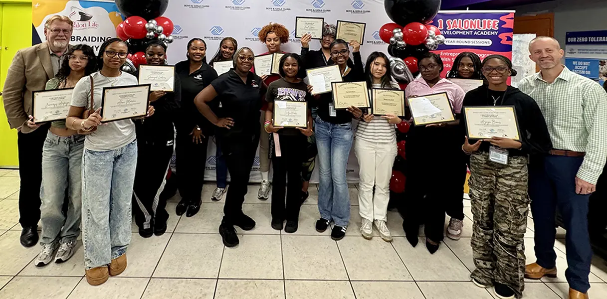 A group picture of the 14 graduates of the Hair Braiding Program proudly showcasing their certificates.