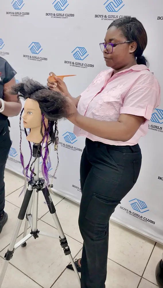 A participant of the hair braiding program parting the hair of their training head
