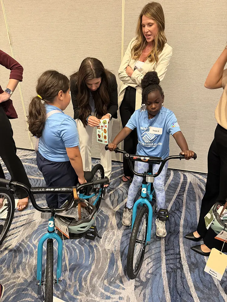 One BGCBC receiving stickers for their bike while another sits on their bike with stickers on the handlebar