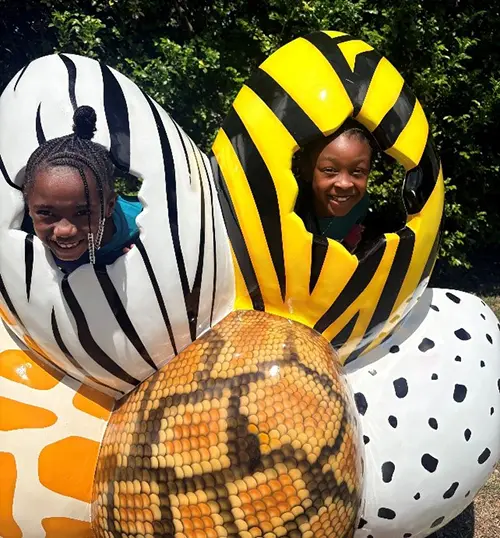 Two Boys & Girls Clubs of Broward County Club Members posing behind photo stand ins that look like animal print covered eggs on the Zoo field trip.