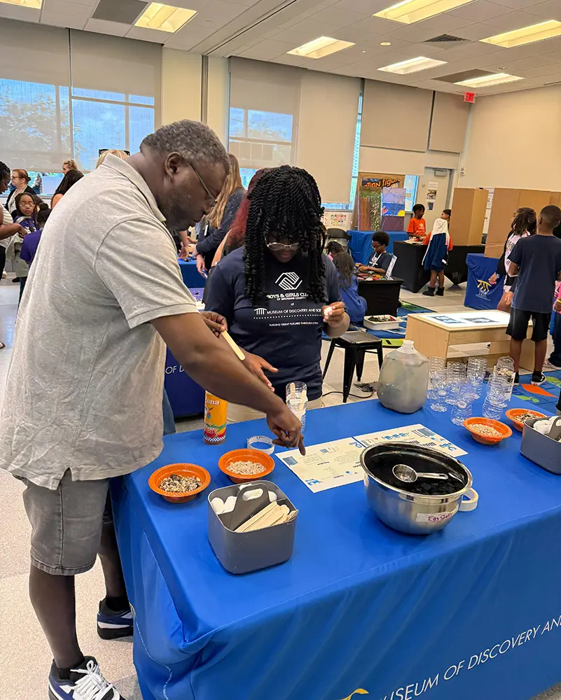 BGCBC Club member working with their Dad on a science project. They are following printed instructions and have materials on the table in front of them.